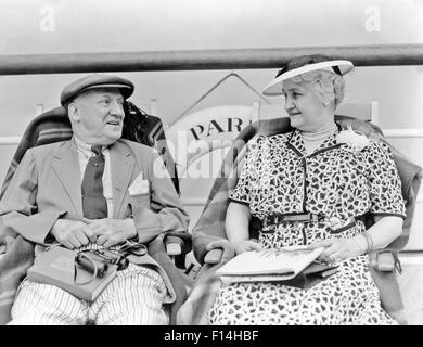 1930s SENIOR COUPLE SITTING IN DECK CHAIRS ON TRANSATLANTIC OCEAN LINER Stock Photo