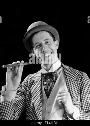 1910s 1920s PORTRAIT SMILING CHARACTER CON MAN BOWLER HAT FANCY SUIT CRAVAT SMOKING CIGAR LOOKING AT CAMERA Stock Photo