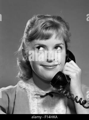 1950s 1960s TEENAGED GIRL TALKING ON TELEPHONE ROLLING EYES SMILING INDOOR Stock Photo