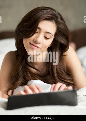 Woman laying on bed using digital tablet Stock Photo