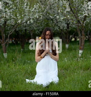 USA, Utah, Provo, Young woman wearing white dress kneeling between trees in blossom