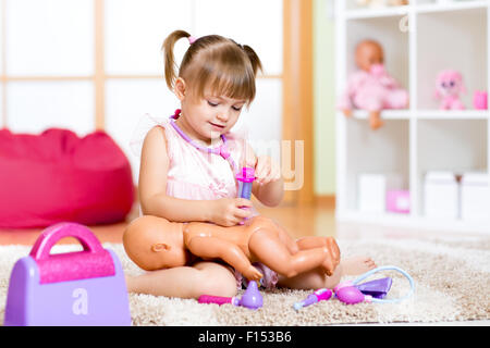 Child in kindergarten. Kid in nursery school. Girl playing doctor with doll in room. Stock Photo
