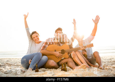 Friends having fun together at the beach, playing guitar and drinking beer Stock Photo