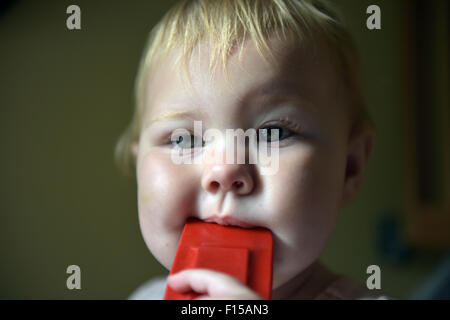 An eleven month old baby chewing on a red plastic kitchen spoon-spatulas to alleviate the pain and discomfort of tooth ache. Stock Photo