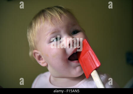 An eleven month old baby chewing on a red plastic kitchen spoon-spatulas to alleviate the pain and discomfort of tooth ache. Stock Photo