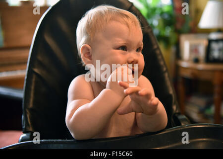 A teething 11 month old baby sitting in a high chair chewing on a slice of apple. Stock Photo