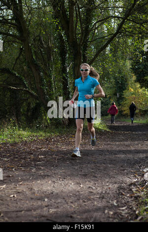 Female running along rural trail in woodland landscape Stock Photo