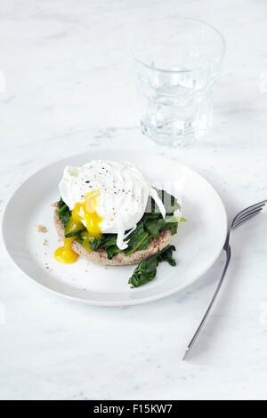 Poached egg with soft yolk and spinach on english muffin, on plate with fork and glass of water, studio shot on white background Stock Photo