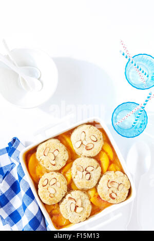 Peach almond cobbler with blue checkered napkin and blue cups with straws, studio shot on white background Stock Photo
