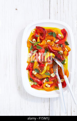 Marinated roasted peppers with garlic and herbs, serving spoon and fork on white wood table, studio shot on white background Stock Photo