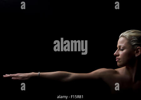 dramatic studio portrait of fit blonde female athlete eyes closed with one outstretched arm across bottom of all black frame Stock Photo