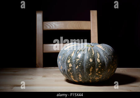 Solitary pumpkin on rustic pine table with chair for Halloween or Thanksgiving preparations. Stock Photo