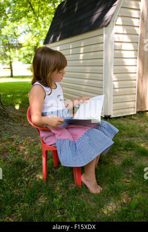 6 year old girl reading under a tree in her front yard Stock Photo