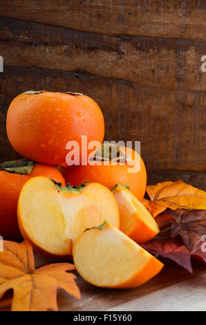 Stack of Autumn harvest fruit, persimmons, on rustic wood background.