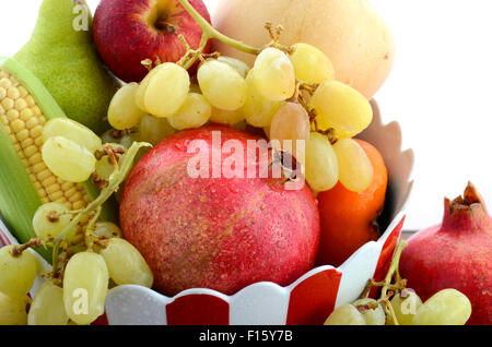 Bowl of Thanksgiving fall fruit and vegetables with pomegranates, persimmons, apples, grapes, and corn in red and white ceramic  Stock Photo