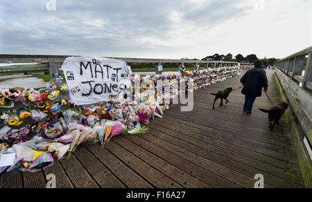 Shoreham, Sussex, UK. 28th August, 2015. A woman walking her dogs early this morning passes the thousands of floral tributes and messages which line the old toll bridge crossing the River Adur at Shoreham to remember those who died in the Shoreham Airshow disaster last weekend  It is almost a week after a Hawker Hunter jet flown by pilot Andrew Hill crashed on to the A27 during a display in the Shoreham Airshow killing 11 people  Credit:  Simon Dack/Alamy Live News Stock Photo