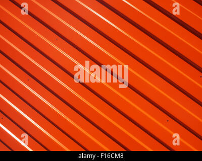 Orange metal corrugated sheet metal closeup with longitudinal stripes and striped shadows illuminated bright sun to use as backg Stock Photo