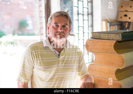 Bookbinder standing in workshop next to a pile of large books Stock Photo