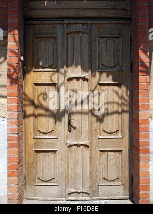 Old wooden door of unpainted wood with curly strips. The upper part of the door is in the shadow of the metal canopy. Photograph Stock Photo