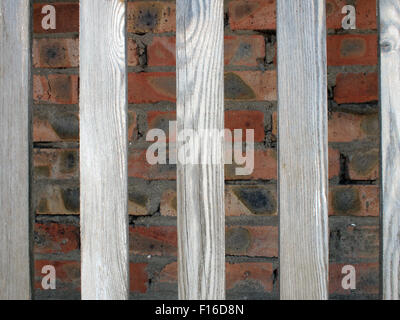 Gray unpainted wooden planks with natural texture on the background wall of red brick. Between boards have large gaps, they are Stock Photo