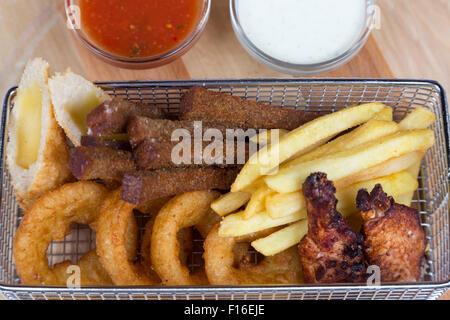 mix from snacks for beer in metal basket serving with sauces on wooden board Stock Photo
