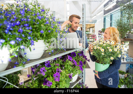 Customer With Flower Pot Looking At Florist Using Mobile Phone Stock Photo