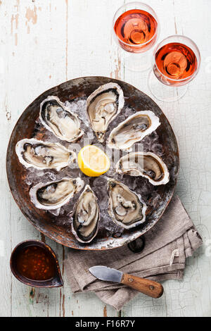 Opened Oysters on metal copper plate on blue wooden background with spicy sauce and wine rose Stock Photo