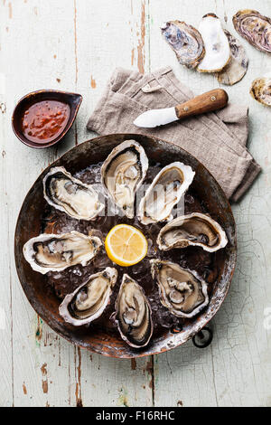 Opened Oysters on metal copper plate on blue wooden background with spicy sauce and oyster knife Stock Photo
