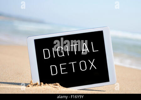 a tablet computer with the text digital detox written in its screen, placed in the sand of a beach Stock Photo