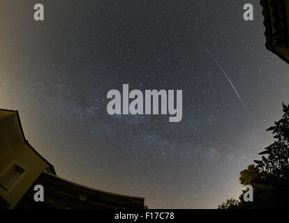 A satellite flares in the night sky with stars of the Milky Way Stock Photo