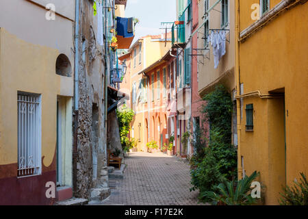 Sunny narrow street with colorful old buildings and green potted plants in medieval town Villefranche-sur-Mer on French Riviera, Stock Photo