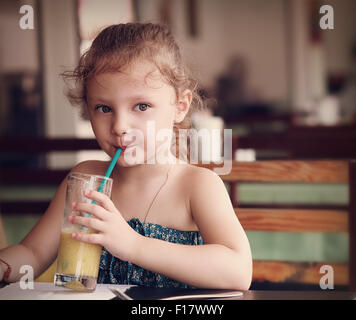 Cute thinking kid girl drinking juice in cafe with serious look. Closeup portrait Stock Photo