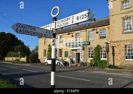 North Riding, York signpost and couple with car outside The Worlsey Arms Hotel, Hovingham, North Yorkshire, UK Stock Photo