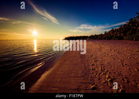 Footprints on the tropical beach at sunset with sun over ocean Stock Photo