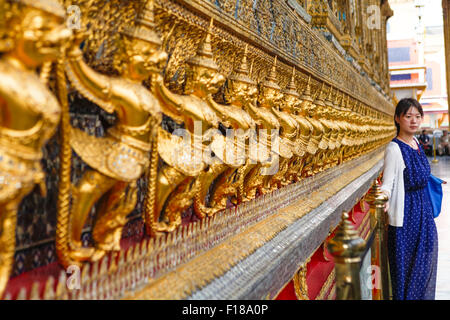 A tourist posing for a photo in front of mythological garuda and naga sculptures at Wat Phra Kaew inside Grand Palace complex in Bangkok, Thailand. Stock Photo