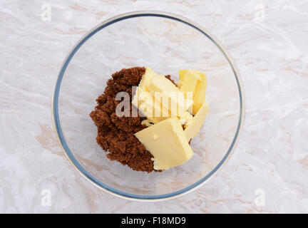 Pats of butter with dark soft sugar in a glass bowl on a marble effect kitchen surface Stock Photo