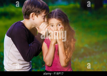 girl whispering in the ear of the boy tells the secret hearings Stock Photo