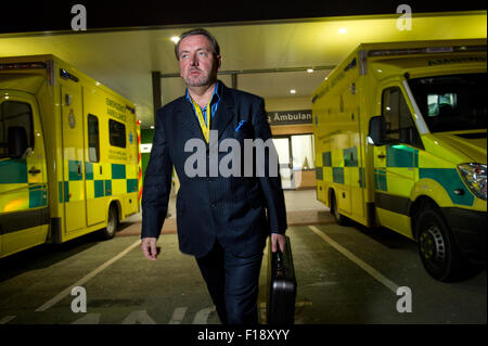 A male out-of-hours doctor, on call, holding medical bag and mobile phone, walking past a line of ambulances at a hospital UK GP Stock Photo