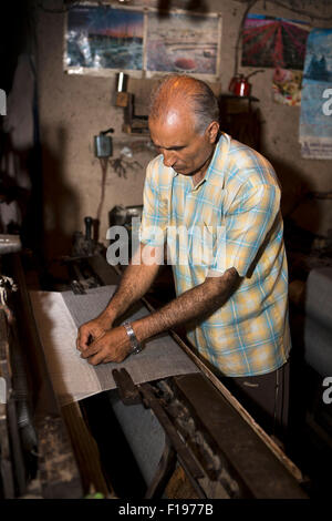 India, Jammu & Kashmir, Srinagar, pashmina production, man weaving pasminas on mechanical loom in dark workshop Stock Photo