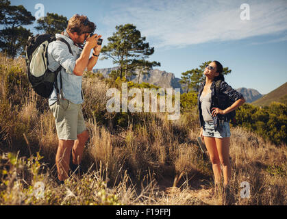Outdoor shot of tourist couple hiking and taking photos with camera. Man taking picture of girlfriend in countryside. Couple on Stock Photo