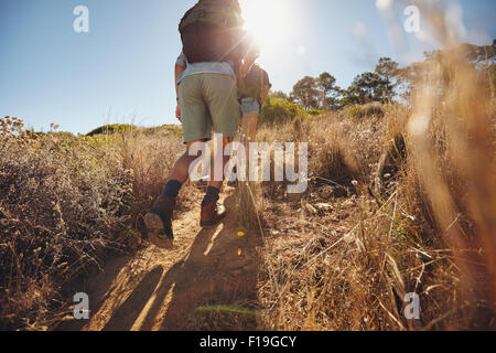 Low angle view of two young people climbing uphill on a mountain. Couple on a hiking trip on a sunny day. Stock Photo