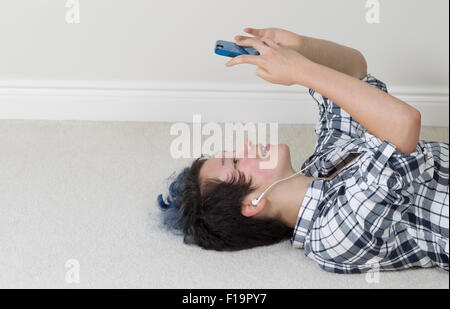 Teen girl looking at cell phone while lying on her back listening to music at home. Stock Photo