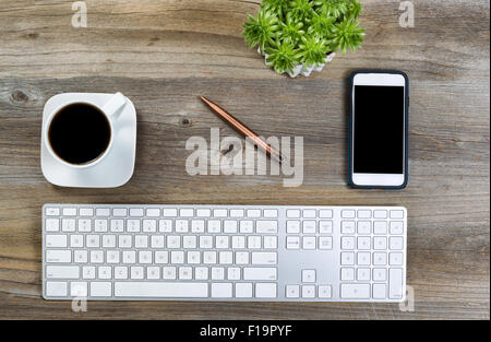 Top view of a neat desktop with keyboard, black coffee, green plant and cell phone on wooden desk. Stock Photo