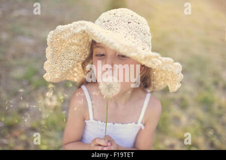 Young girl in a hat blowing dandelion Stock Photo