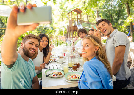 Portrait of a cheerful friends making selfie photo on smartphone in outdoor restaurant Stock Photo
