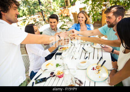 Group of a young friends making toast around table at dinner party in outdoor restaurant Stock Photo
