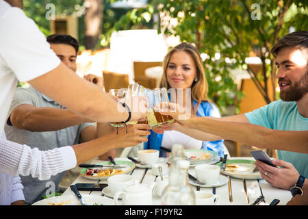 Group of a cheerful friends making toast around table at dinner party in outdoor restaurant Stock Photo