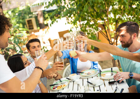 Group of a friends making toast around table at dinner party in outdoor restaurant Stock Photo