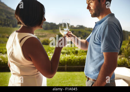 Closeup shot of young couple toasting wine while standing outdoors at winery restaurant with vineyard in background. Man and wom Stock Photo