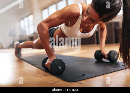 Gym woman doing push-up exercise with dumbbell. Strong female doing crossfit workout. Stock Photo